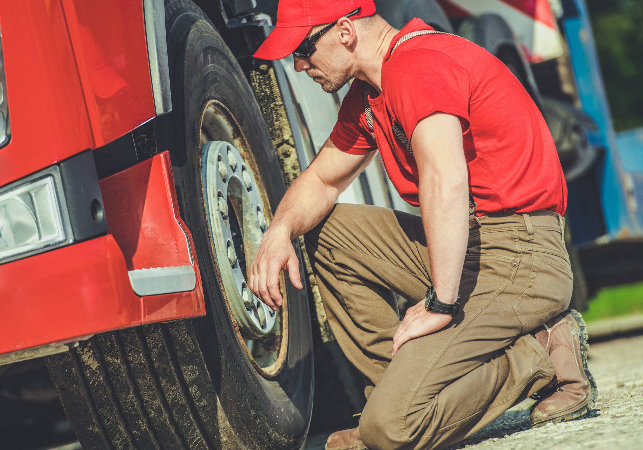 Truck Mechanic Inspecting Tire Of A Red Truck On A Sunny Day In A Service Area