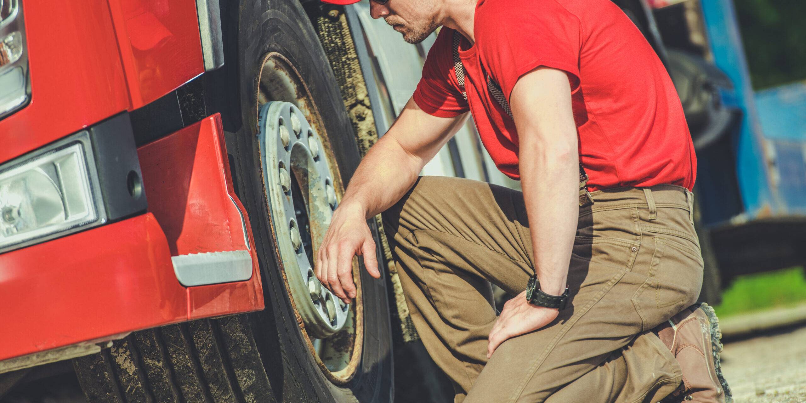 Truck Mechanic Inspecting Tire Of A Red Truck On A Sunny Day In A Service Area